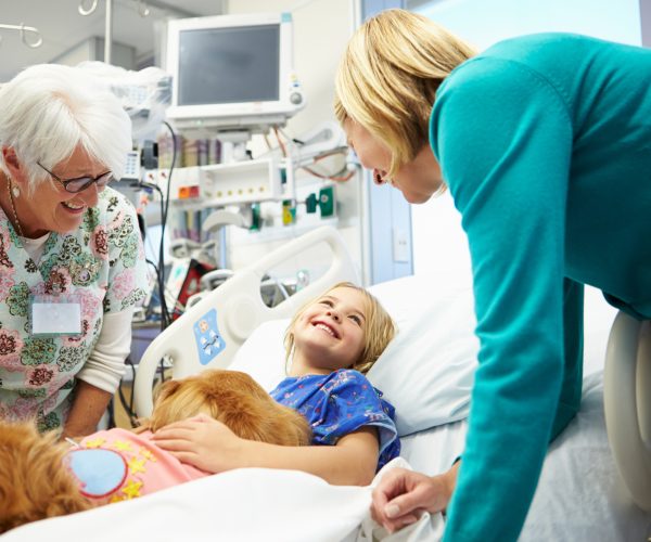 Young Girl Being Visited In Hospital By Therapy Dog And Family